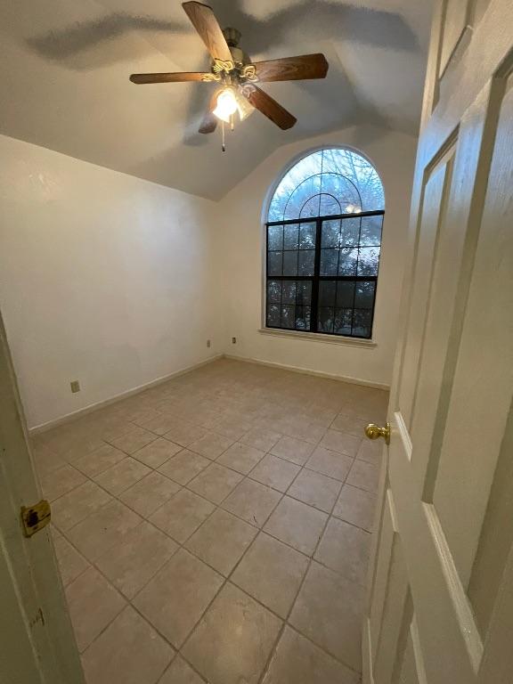 unfurnished room featuring light tile patterned flooring, vaulted ceiling, baseboards, and ceiling fan