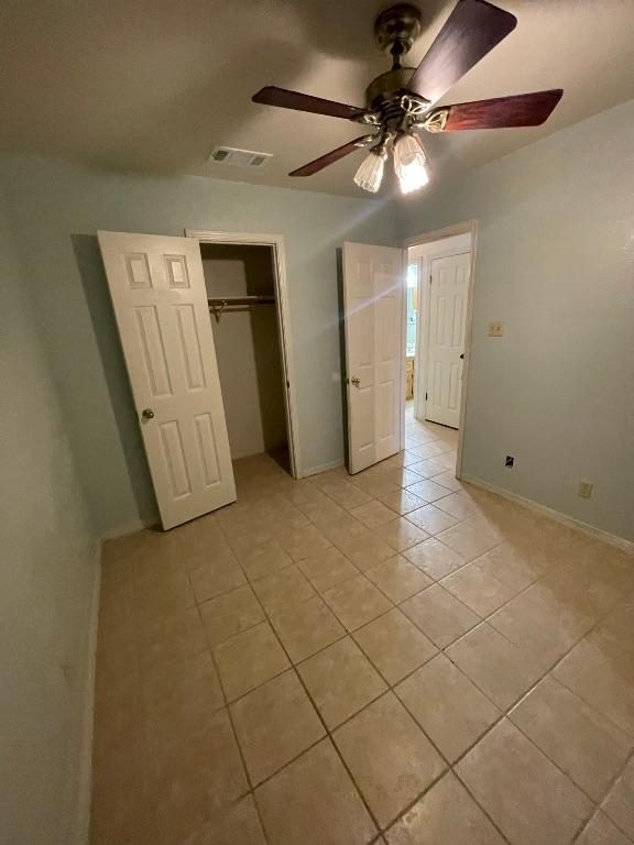 unfurnished bedroom with light tile patterned floors, visible vents, baseboards, ceiling fan, and a closet