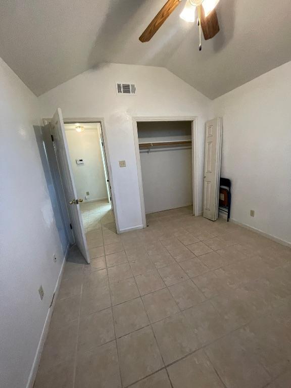 unfurnished bedroom featuring ceiling fan, light tile patterned floors, visible vents, vaulted ceiling, and a closet