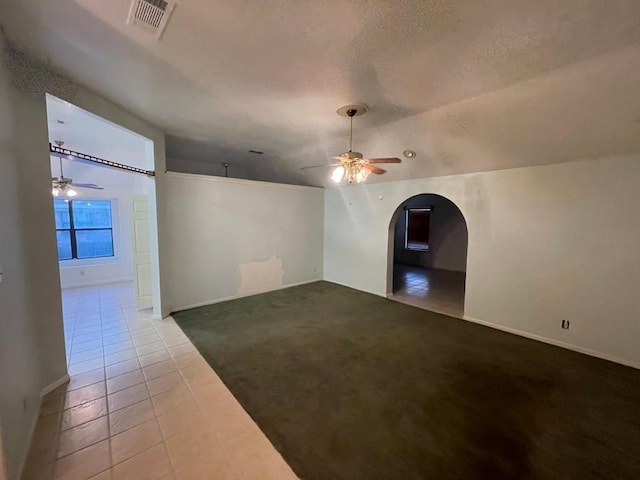 carpeted empty room with a textured ceiling, arched walkways, a ceiling fan, and tile patterned floors