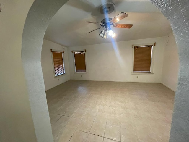 empty room with lofted ceiling, arched walkways, and a ceiling fan