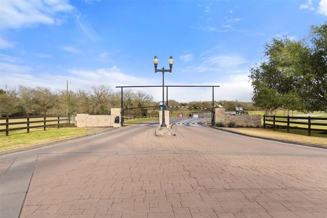 view of road featuring street lighting, a gated entry, a gate, and curbs