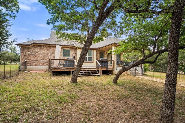 rear view of house featuring a lawn, fence, a wooden deck, and brick siding