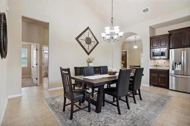 dining space featuring light tile patterned flooring, a notable chandelier, arched walkways, high vaulted ceiling, and visible vents