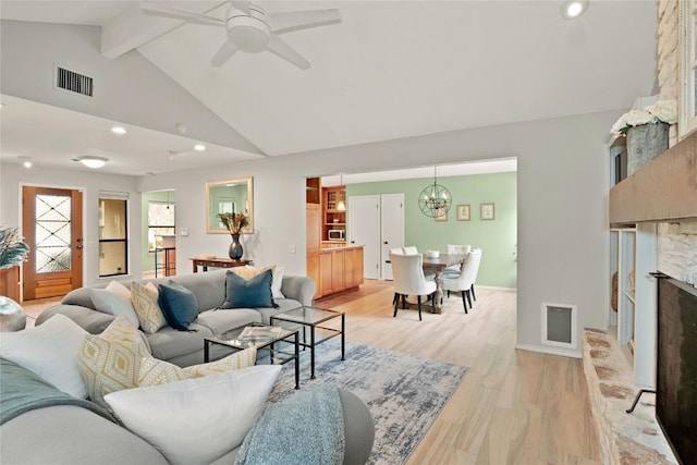 living room with a stone fireplace, visible vents, light wood-style flooring, and beam ceiling