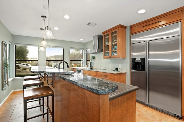 kitchen with stainless steel appliances, brown cabinetry, a sink, and wall chimney exhaust hood