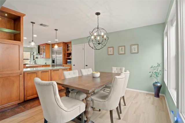 dining space featuring light wood finished floors, visible vents, baseboards, and a notable chandelier