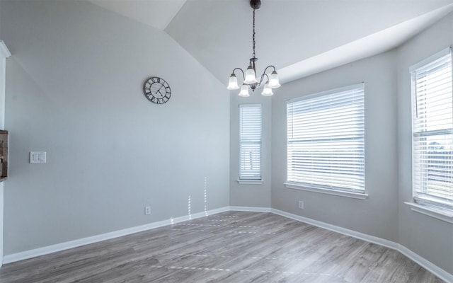 spare room featuring vaulted ceiling, wood finished floors, a notable chandelier, and baseboards