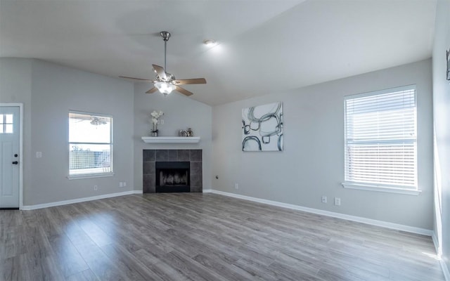 unfurnished living room featuring lofted ceiling, ceiling fan, wood finished floors, a tile fireplace, and baseboards