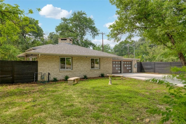 back of house with driveway, a chimney, an attached garage, fence, and a yard