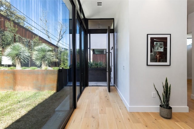 doorway to outside featuring light wood-style floors, visible vents, baseboards, and a wall of windows