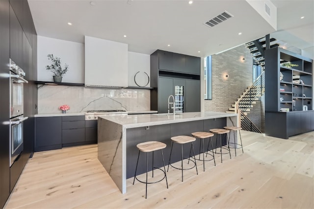 kitchen with a breakfast bar, built in refrigerator, visible vents, a large island, and modern cabinets