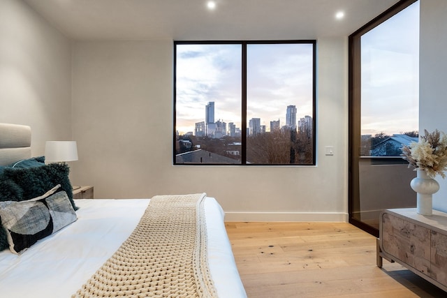 bedroom featuring wood-type flooring, a view of city, baseboards, and recessed lighting