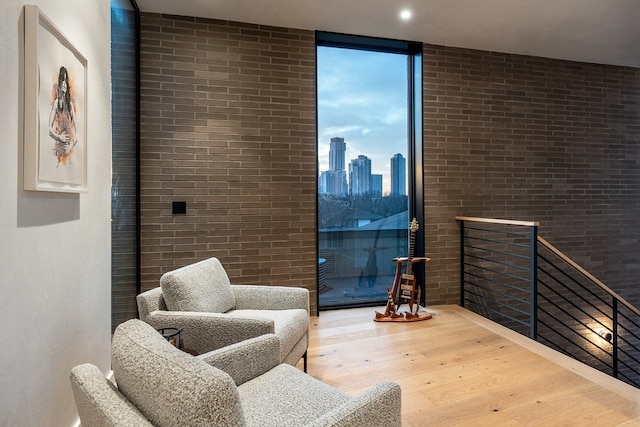 living area with a view of city, brick wall, wood finished floors, and floor to ceiling windows