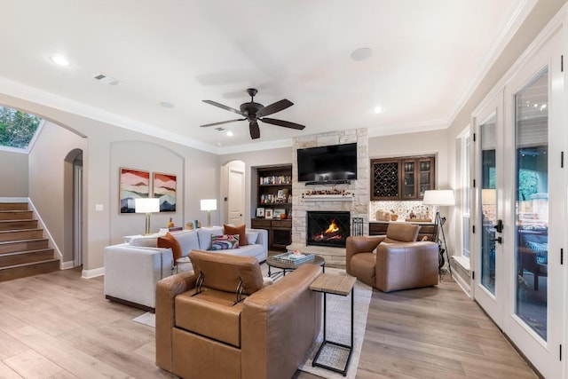 living area featuring arched walkways, crown molding, light wood finished floors, stairway, and a stone fireplace