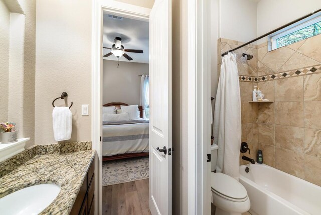 ensuite bathroom with connected bathroom, toilet, wood finished floors, vanity, and shower / bath combination with curtain