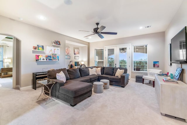 living room featuring arched walkways, french doors, light colored carpet, visible vents, and a ceiling fan