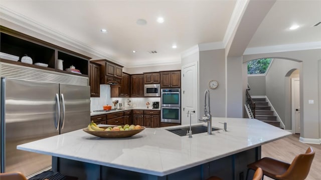 kitchen featuring built in appliances, arched walkways, a sink, a kitchen bar, and crown molding