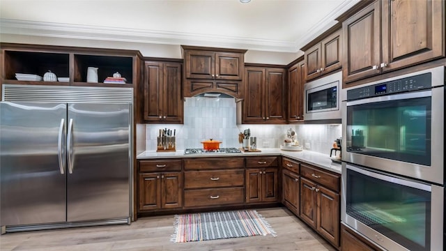 kitchen featuring built in appliances, light countertops, backsplash, and crown molding