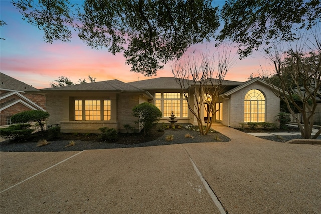 view of front of home with brick siding, driveway, and roof with shingles