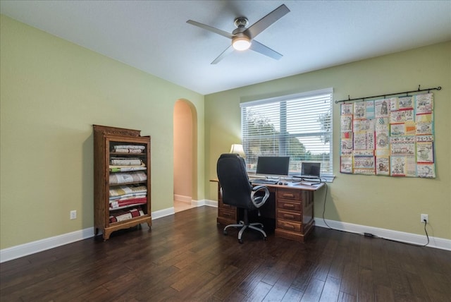 office area with dark wood-style floors, baseboards, arched walkways, and a ceiling fan