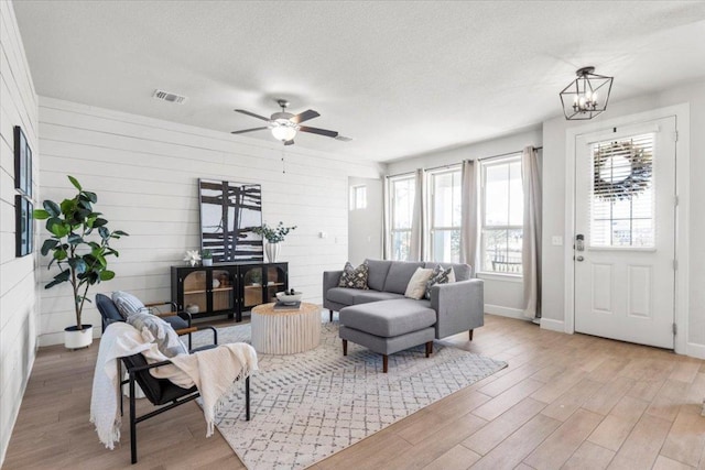 living area with ceiling fan with notable chandelier, visible vents, a textured ceiling, and wood finished floors