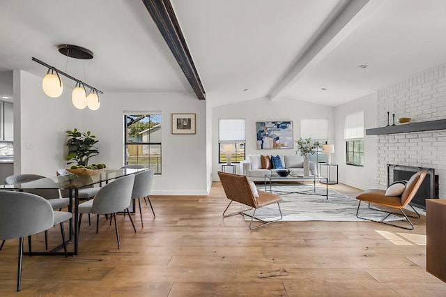 dining area with light wood-type flooring, a brick fireplace, vaulted ceiling with beams, and baseboards