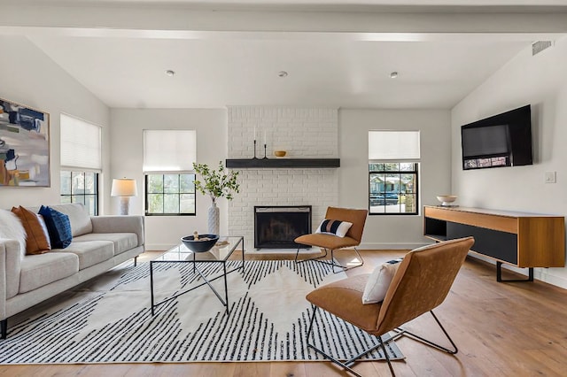 living area with visible vents, lofted ceiling with beams, light wood-style flooring, a brick fireplace, and a wealth of natural light