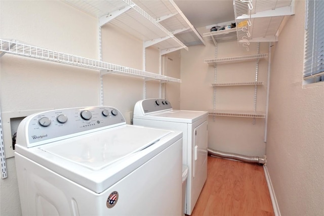 clothes washing area featuring laundry area, baseboards, light wood-style floors, and washer and dryer