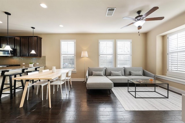 living area with dark wood-style floors, baseboards, visible vents, and a healthy amount of sunlight