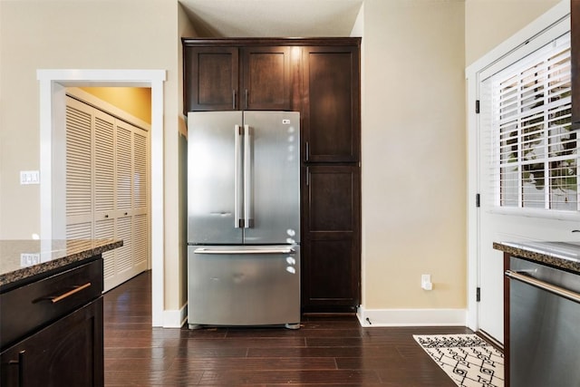 kitchen with stone counters, dark brown cabinetry, stainless steel appliances, baseboards, and dark wood-style floors