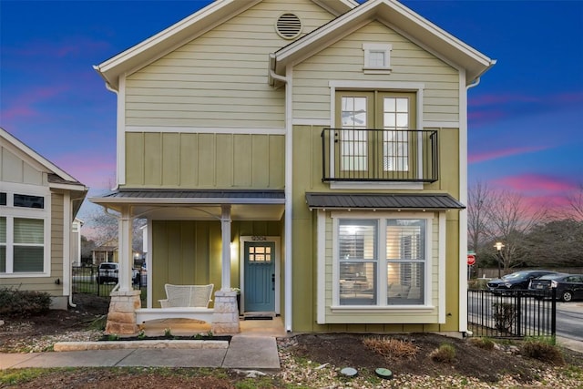 view of front of property featuring board and batten siding, covered porch, fence, and metal roof