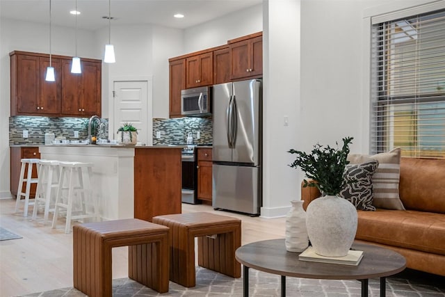 kitchen with light wood finished floors, pendant lighting, stainless steel appliances, and backsplash