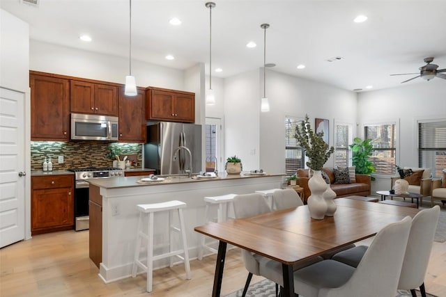 kitchen featuring hanging light fixtures, tasteful backsplash, appliances with stainless steel finishes, and light wood-style flooring