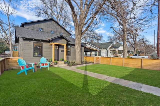 view of front of home featuring fence private yard, roof with shingles, and a front yard