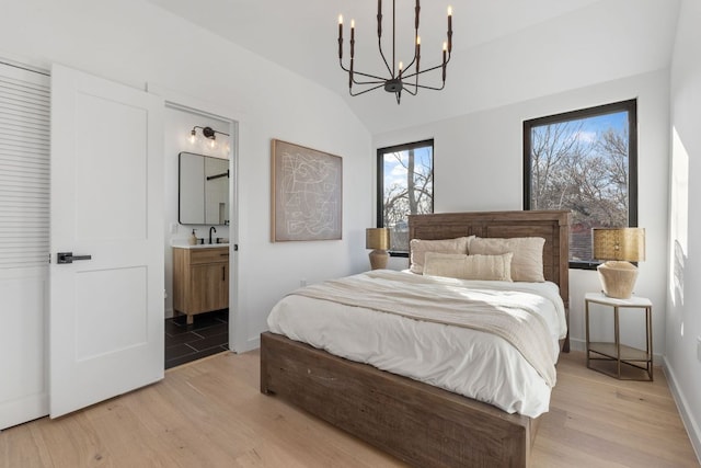 bedroom featuring lofted ceiling, a sink, light wood-style flooring, and ensuite bathroom