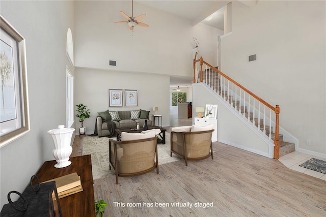 living area with a high ceiling, wood finished floors, visible vents, a ceiling fan, and stairway