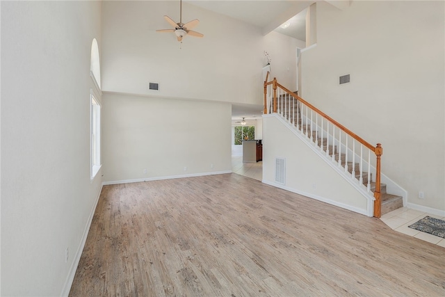 unfurnished living room featuring stairway, a high ceiling, a ceiling fan, wood finished floors, and baseboards