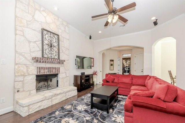 living room with arched walkways, ornamental molding, a stone fireplace, wood finished floors, and baseboards