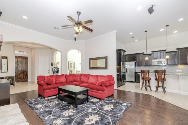 living room with light wood-style floors, arched walkways, visible vents, and crown molding