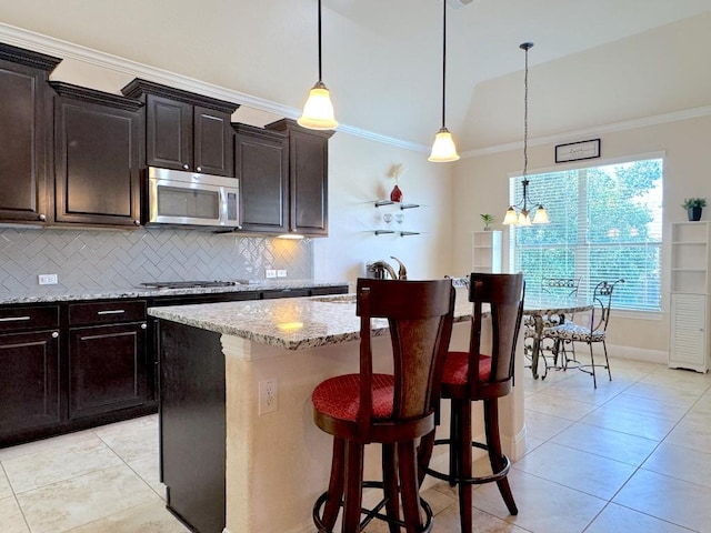 kitchen featuring light stone counters, stainless steel appliances, backsplash, ornamental molding, and a kitchen breakfast bar