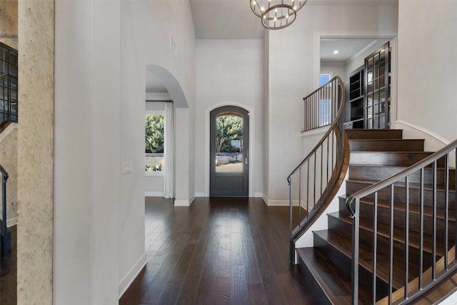 foyer entrance featuring arched walkways, a high ceiling, baseboards, stairway, and wood-type flooring