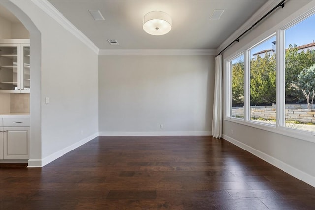 spare room featuring plenty of natural light, visible vents, dark wood-style flooring, and ornamental molding