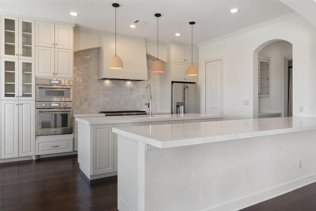 kitchen featuring a kitchen island with sink, dark wood-style flooring, light countertops, appliances with stainless steel finishes, and tasteful backsplash