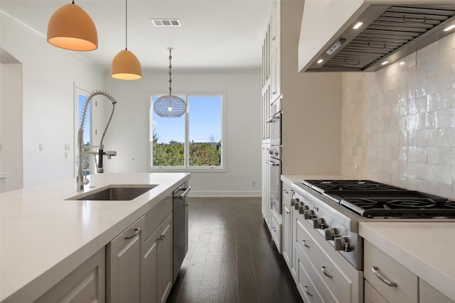 kitchen with visible vents, appliances with stainless steel finishes, light countertops, wall chimney range hood, and a sink