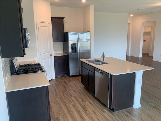 kitchen with a kitchen island with sink, stainless steel appliances, light countertops, light wood-type flooring, and a sink