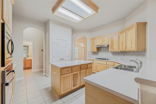 kitchen with under cabinet range hood, light brown cabinets, stainless steel oven, and a sink