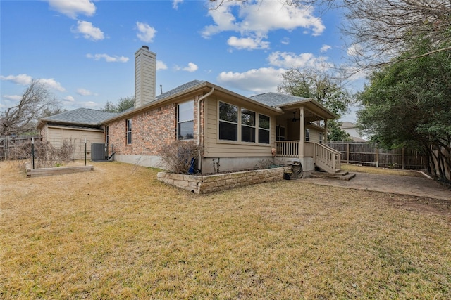 rear view of house featuring brick siding, a yard, a chimney, fence, and cooling unit