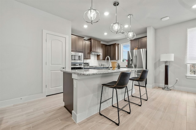 kitchen with appliances with stainless steel finishes, dark brown cabinetry, a center island with sink, and light wood finished floors