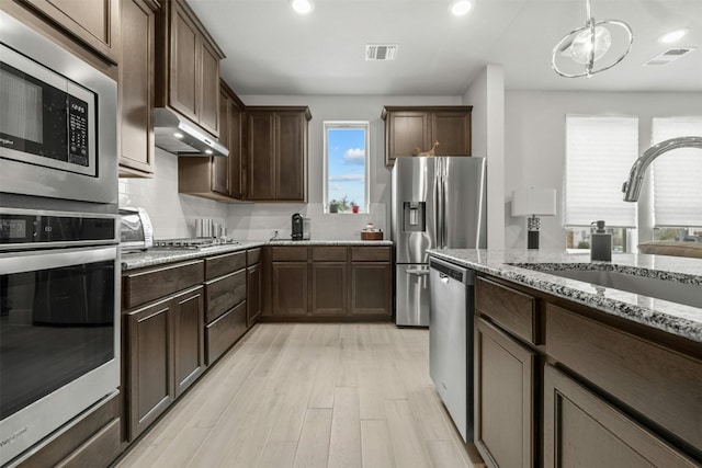 kitchen with light stone counters, under cabinet range hood, a sink, visible vents, and appliances with stainless steel finishes